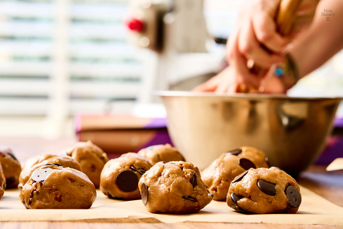 Bolletjes chocoladekoekjesdeeg op een houten plank met een persoon op de achtergrond.
