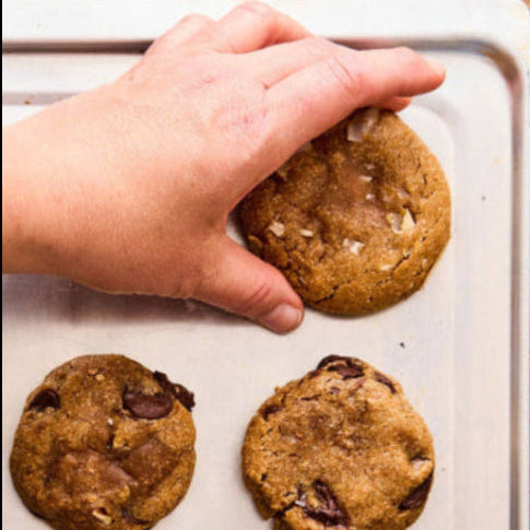 een dienblad met koekjes uit de oven en een hand die één koekje uitkiest