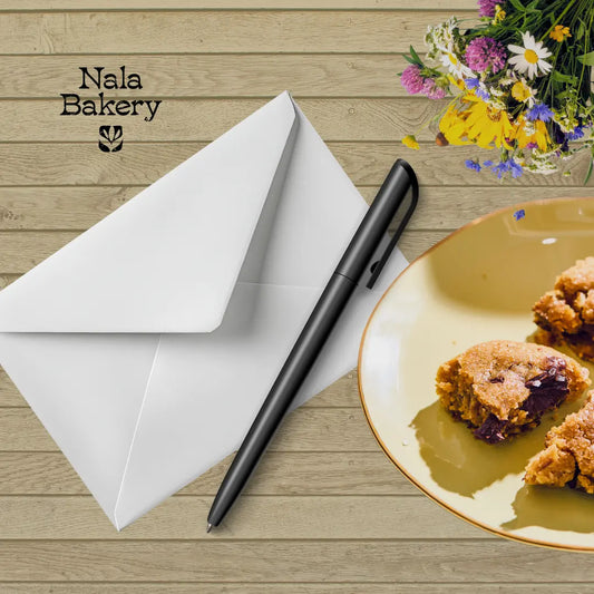 Witte envelop, zwarte pen en een bord met koekjes op een houten ondergrond met het logo van Nala Bakery.