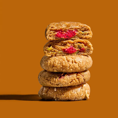 Stapel pistachekoekjes met frambozenvulling op een goudbruine achtergrond.