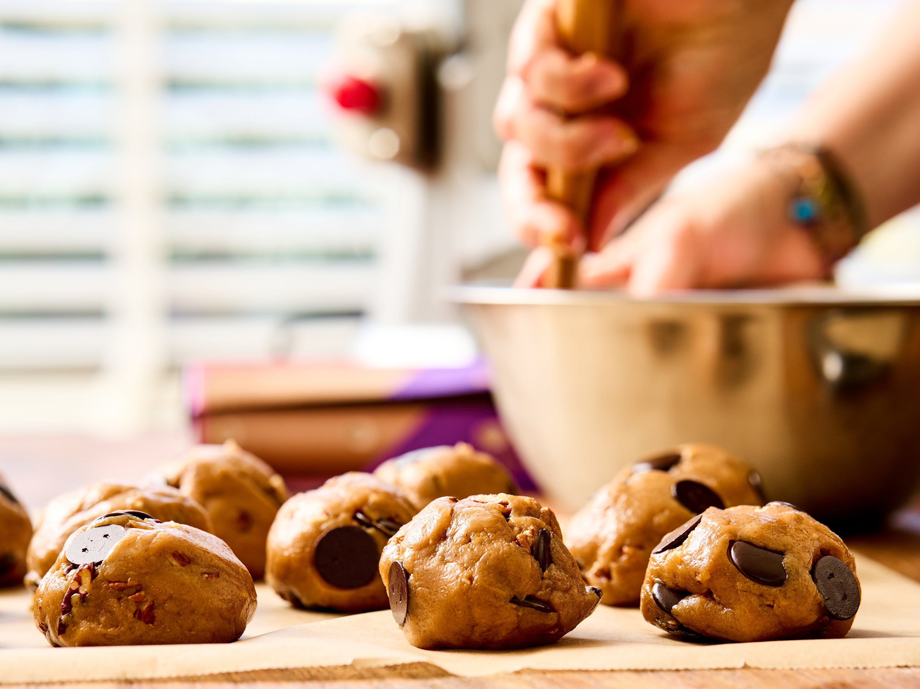 Bolletjes chocoladekoekjesdeeg op een houten plank met een persoon op de achtergrond.